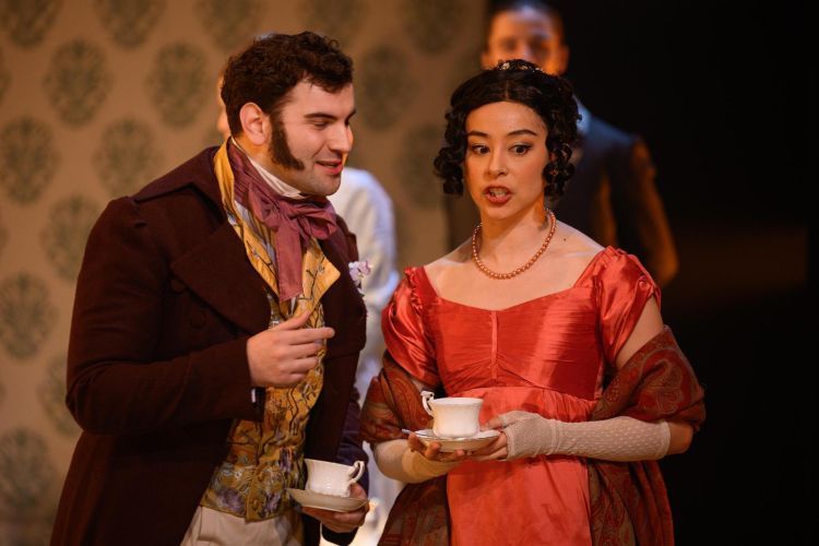 Male and Female Opera singer in colourful flamboyant Victorian style costumes holding white teacups and saucers